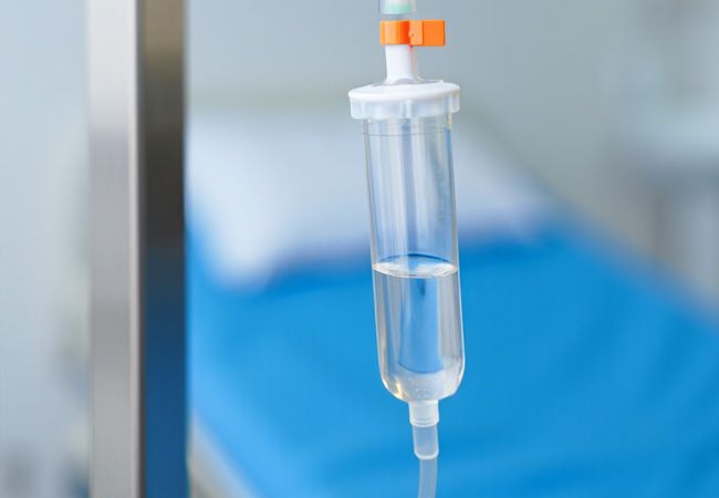 Инфузионный мешок с прозрачной жидкостью и медицинской маркировкой висит на металлической стойке в больничной палате